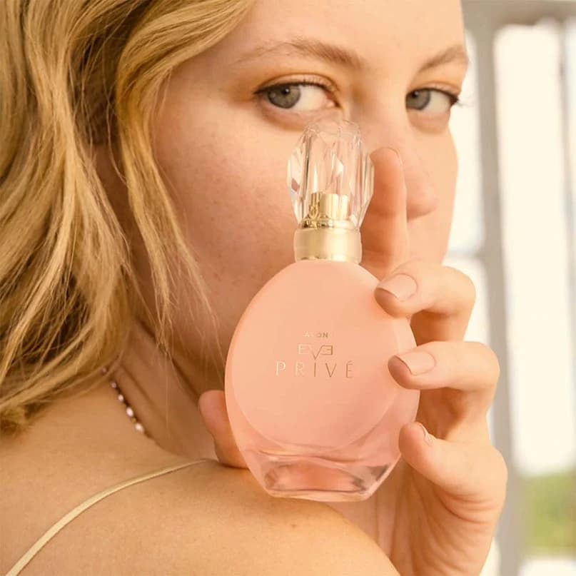 a model holding avon eve prive perfume bottle on shoulder